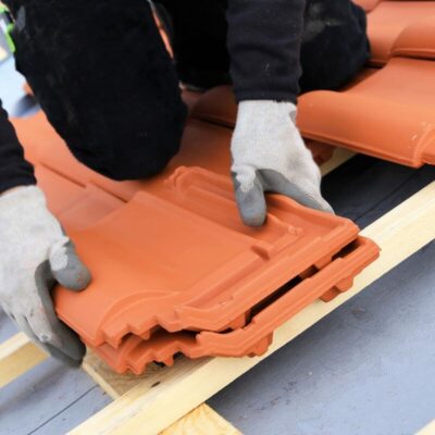 Osoba układa dachówki ceramiczne na drewnianej konstrukcji.
