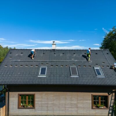 Trzech pracowników wykonuje prace na dachy domu z szarymi dachówkami.