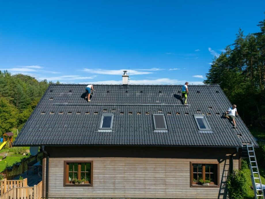 Trzech pracowników wykonuje prace na dachy domu z szarymi dachówkami.